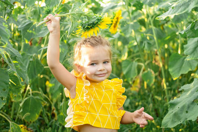 Happy little kid girl playing in blooming sunflower field on sunny summer day