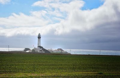 Agricultural field by pigeon point lighthouse against cloudy sky