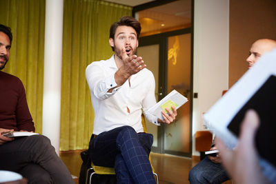 Shocked businessman discussing with colleagues while sitting in office seminar