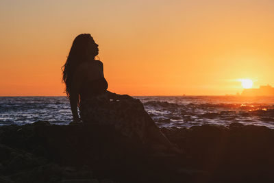 Silhouette man looking at sea against sky during sunset