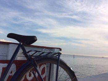 Close-up of bicycle by sea against sky