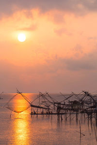 Silhouette fishing net by sea against sky during sunset