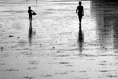 Silhouette people walking on wet beach