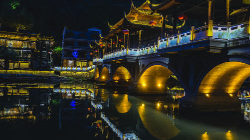 Illuminated bridge over river in city at night