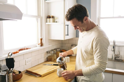 Happy man pouring coffee while standing by kitchen counter at home