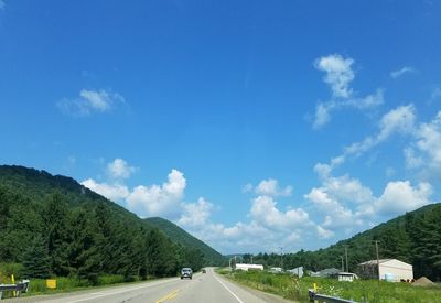 Road by trees against blue sky