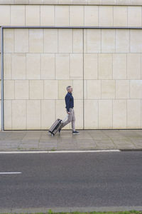 Businessman with suitcase walking on footpath by wall