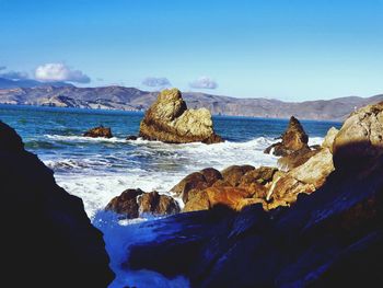 Rocks on sea shore against blue sky