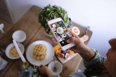 High angle view of woman photographing waffles in plate on table at home