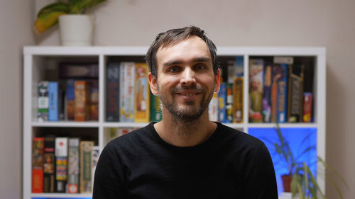 A handsome middle-aged caucasian man in a black sweatshirt smiles as he stands in the room 