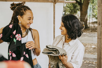 Happy female customers looking at each other while shopping at flea market