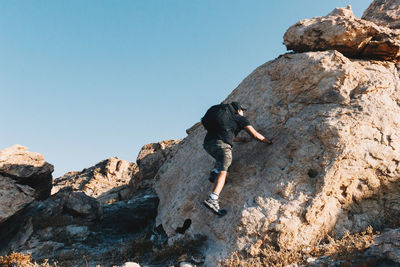 Full length of man climbing on rock against clear sky