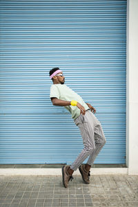 Flexible man dancing on footpath in front of blue shutter