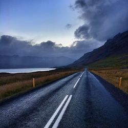 Icelandic road by mountain against cloudy sky at dusk