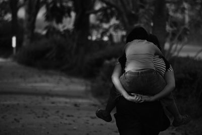 Rear view of mother carrying daughter on road