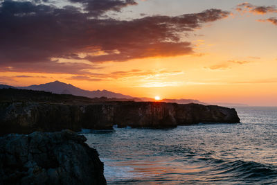 Rock formation on sea against sky during sunset