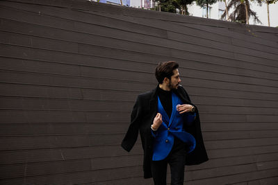 Young man in suit smoking cigarette against wall