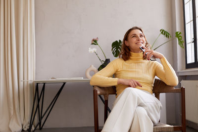 Dreamy woman with smartphone on chair at home