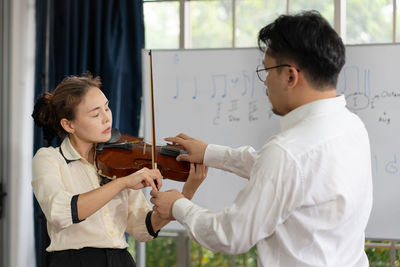 Student learning how to play violin with teacher in classroom