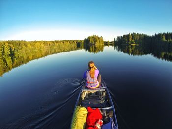 Rear view of women sitting on lake against sky