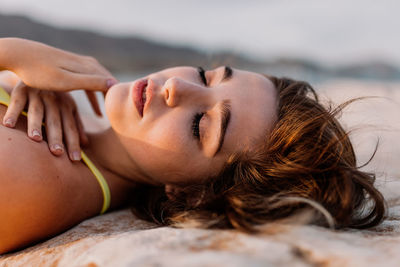 Carefree young woman in yellow bikini lying on rock at beach