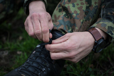 Low section of army soldier tying shoe on grassy field