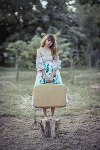 Woman with luggage standing on log