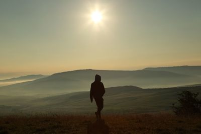 Silhouette person walking on mountain against sky during sunrise