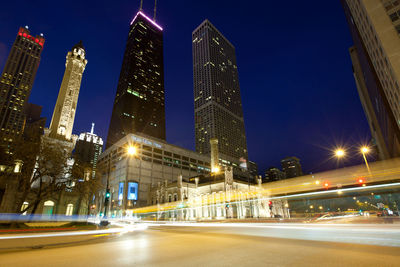 Illuminated city street and buildings against sky at night