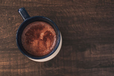 Closeup of hot cocoa drink in blue mug on wooden table.