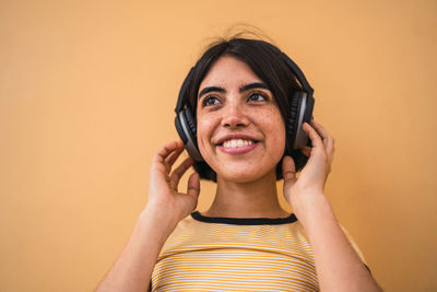 Close-up of smiling woman wearing headphones standing against beige background