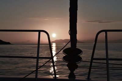 Silhouette railing by sea against sky during sunset