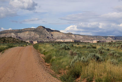 View of dirt road along rocky mountains against cloudy sky