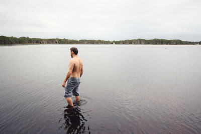 Rear view of shirtless man standing in lake against sky