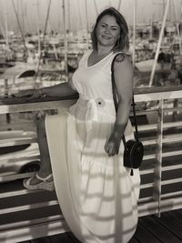 Portrait of smiling woman standing by railing at harbor
