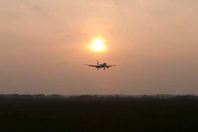 Airplane flying against orange sky at sunset