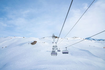 Ski lift moving over scenic snow covered mountain against blue sky