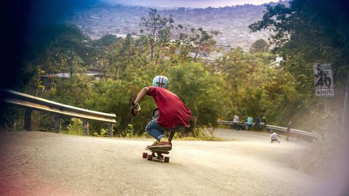 Rear view full length of boy skateboarding on road