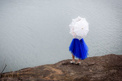 Rear view of woman standing on rock by water