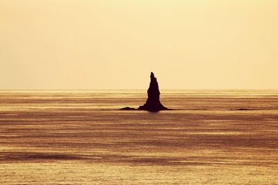 Silhouette man in sea against sky during sunset