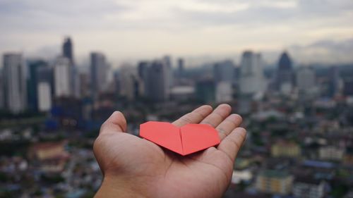 Close-up of person holding hands against buildings in city