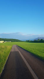 Empty road amidst field against clear blue sky