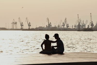 Man and woman sitting on sea against sky