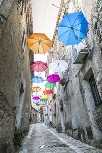 Low angle view of multi colored umbrellas hanging on street amidst buildings