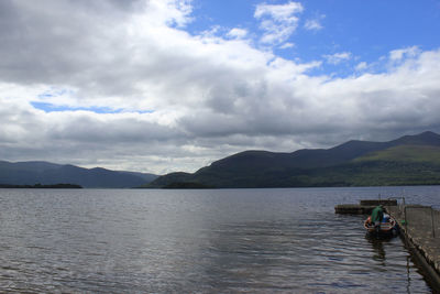 Person walking in lake by boat against cloudy sky