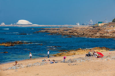 People on beach against clear blue sky