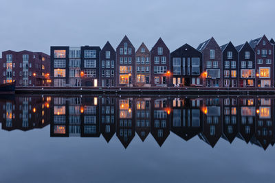 Reflection of illuminated buildings in lake against sky at dusk