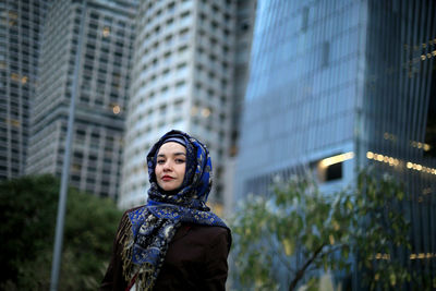 Low angle view of young woman looking away against buildings in city