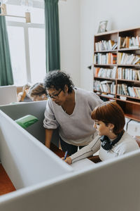 Teacher standing by female teenage student studying in library