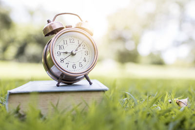 Close-up of alarm clock on book over grass